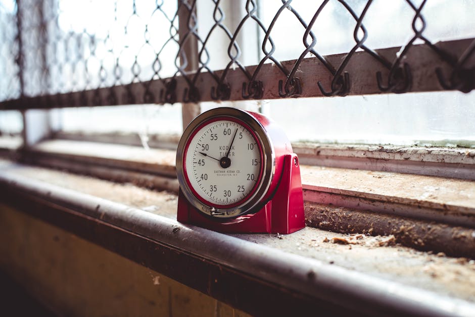 A red timer sits on a dusty windowsill with a chain link fence background, evoking nostalgia.