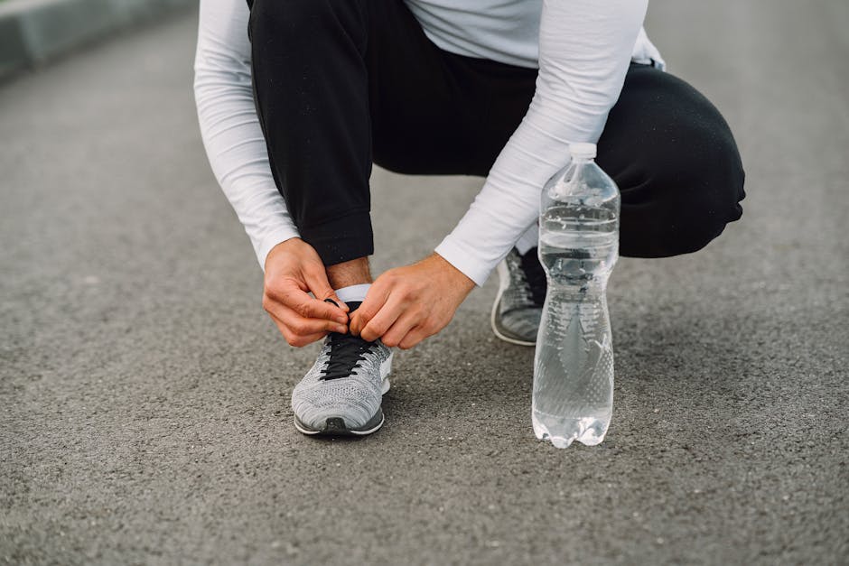Runner tying shoelaces on the road with a water bottle beside. Fitness preparation.
