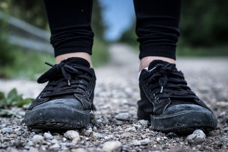 A close-up view of black sneakers on a gravel path outdoors, showcasing casual footwear style.