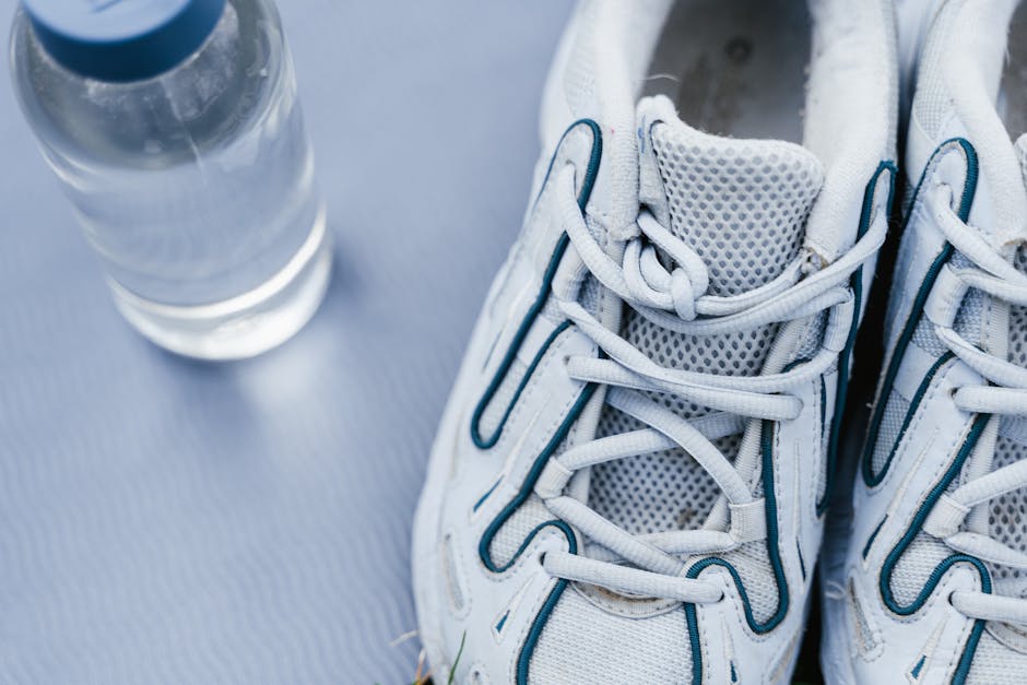 White sneakers with laces next to a clear water bottle on a mat.