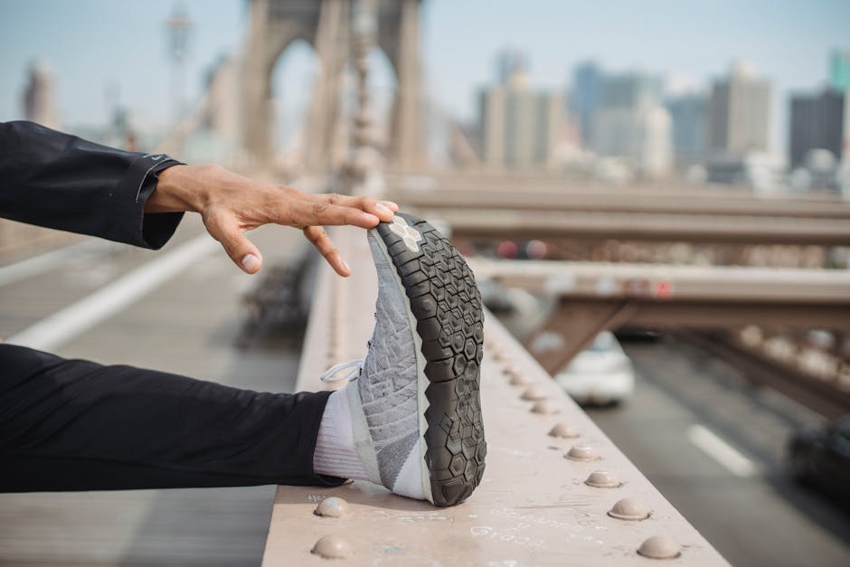 Person stretching on Brooklyn Bridge, focusing on foot with city skyline in background.