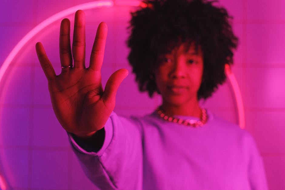 Confident African American female with dark curly hair showing stop gesture in room with bright pink neon light